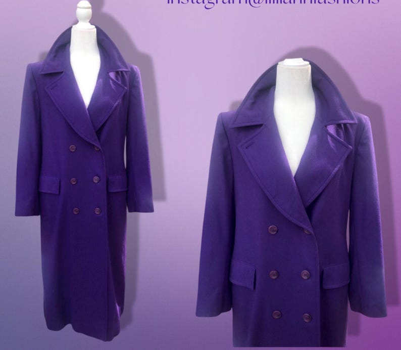 May include: A long, double-breasted purple coat displayed on a mannequin. The coat features a wide collar, two rows of buttons, and two front pockets. The coat is a solid color and appears to be made of a wool or wool-blend fabric.