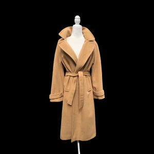 May include: A long, camel-colored coat featuring a wide lapel collar, long sleeves with cuff straps, and a matching tie belt at the waist. The coat is displayed on a white mannequin, showcasing a structured design with two front pockets.