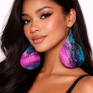 May include: Large teardrop-shaped earrings featuring a vibrant snakeskin pattern in shades of bright pink, deep purple, and electric blue. The earrings have a textured surface and are suspended from silver-toned metal hooks that attach to the earlobes.