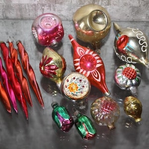 May include: A collection of vintage Christmas ornaments in various shapes and colors. Includes red, pink, and gold teardrop-shaped ornaments, along with round and bulbous designs. Some ornaments have intricate painted details, and all have metal caps for hanging.