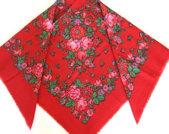 May include: A red square scarf with a floral pattern. The scarf features a vibrant design of pink, red, and purple flowers with green leaves. The edges of the scarf have a fringed trim.
