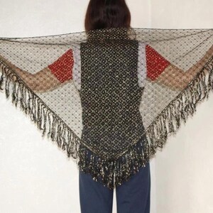 May include: A triangular black lace shawl featuring a delicate dotted pattern and long, flowing fringe along the edges. The fabric is sheer and lightweight, showcasing a dark, intricate design that drapes across the shoulders and back.