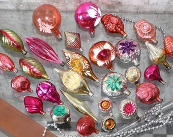 May include: A collection of vintage glass Christmas ornaments in various shapes and sizes, including spheres, teardrops, and finials. The ornaments feature vibrant shades of pink, red, gold, green, and silver, with some displaying painted floral details.