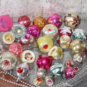 May include: A collection of assorted vintage glass Christmas ornaments in various shapes, sizes, and colors including pink, gold, silver, red, and teal. Many feature indented centers, painted floral details, glitter accents, and metallic finishes.