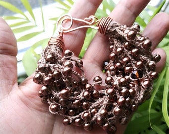 May include: A handmade bracelet featuring brown beads and a crocheted design. The bracelet has a copper-colored clasp and wire accents. The beads are small and round, giving the bracelet a delicate appearance. The overall style is bohemian.