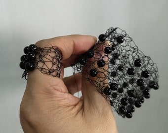 May include: A black wire mesh bracelet and a matching ring, both featuring a delicate, open-weave construction adorned with small, glossy black spherical beads integrated throughout the intricate, web-like wire structure of the jewelry set.