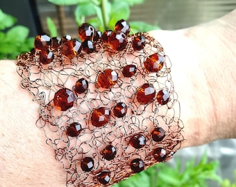 May include: A copper-colored wire cuff bracelet with amber-colored beads. The bracelet has a woven design with multiple faceted beads of varying sizes. The beads are a deep, rich brown color, and the wire has a metallic sheen.