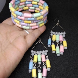 May include: A pastel-colored bracelet and earrings set. The bracelet is a coil design with rows of cylindrical beads in shades of pink, yellow, blue, and green. The earrings have a triangular wire frame with dangling beads in matching colors.
