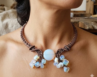 May include: A wire-wrapped copper choker necklace featuring a central round iridescent opal-like stone. The design includes multiple smaller, irregular tumbled stones in similar milky white tones suspended from the copper wire framework.