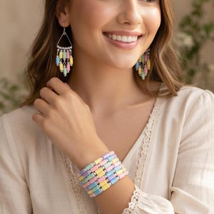 May include: A woman wearing pastel-colored jewelry. The jewelry includes a bracelet and earrings. The bracelet is made of rectangular beads in shades of pink, yellow, blue, and lavender. The earrings have a similar design, with dangling beads.