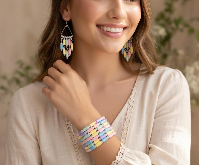 May include: A woman wearing pastel-colored jewelry. The jewelry includes a bracelet and earrings. The bracelet is made of rectangular beads in shades of pink, yellow, blue, and lavender. The earrings have a similar design, with dangling beads.