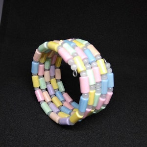 May include: A pastel-colored bracelet with cylindrical beads in shades of pink, yellow, blue, and purple. The bracelet is coiled and appears to be made of multiple strands. The beads are strung together with a thin, flexible wire.