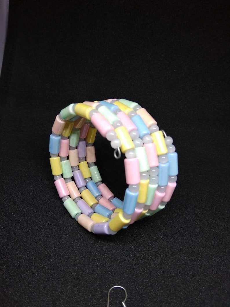 May include: A pastel-colored bracelet with cylindrical beads in shades of pink, yellow, blue, and purple. The bracelet is coiled and appears to be made of multiple strands. The beads are strung together with a thin, flexible wire.