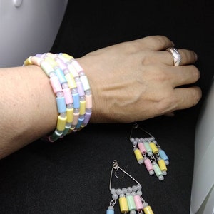 May include: A multi-strand bracelet and a pair of matching dangle earrings featuring cylindrical beads in pastel shades of pink, yellow, blue, and green, interspersed with small white round spacer beads on silver-toned metal findings.