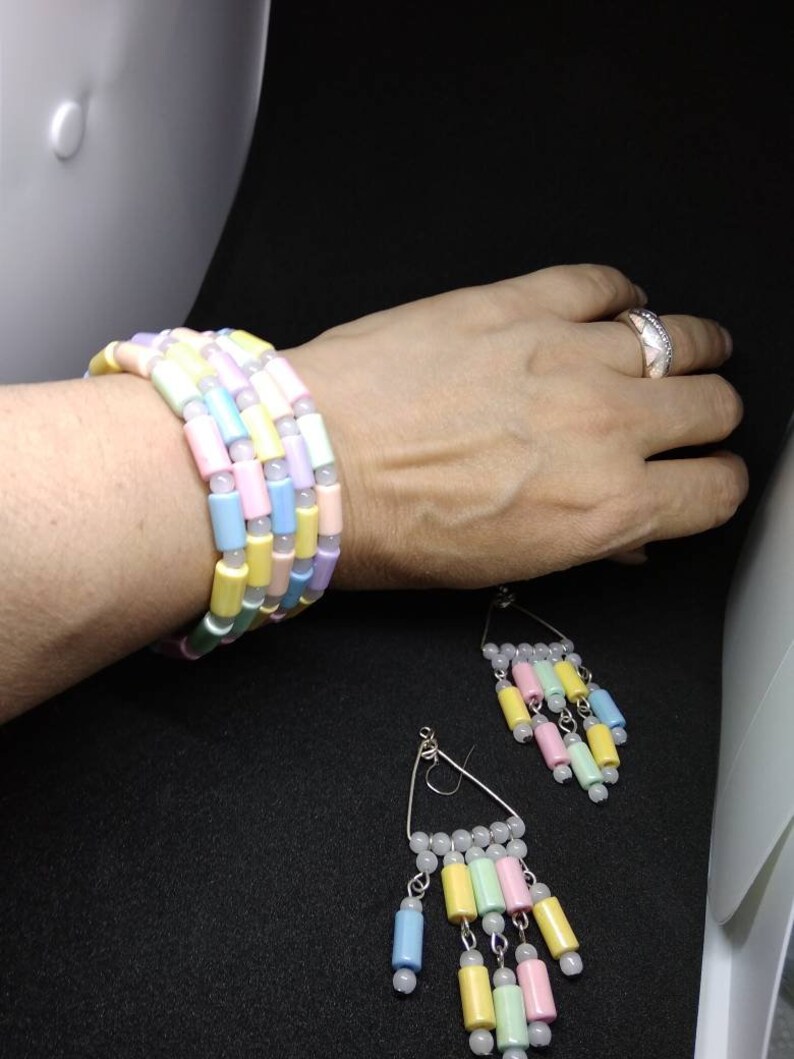 May include: A multi-strand bracelet and a pair of matching dangle earrings featuring cylindrical beads in pastel shades of pink, yellow, blue, and green, interspersed with small white round spacer beads on silver-toned metal findings.
