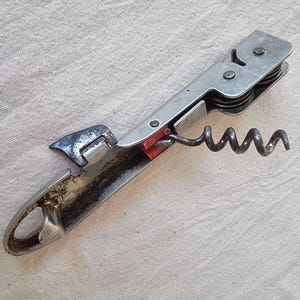 以下が含まれることがあります： ボトルオープナー付きのヴィンテージメタルコルクスクリュー。コルクスクリューは、赤いアクセントとスパイラルワームを備えたシルバー仕上げです。ワインボトルのコルクを取り外すように設計されています。