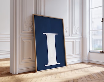 以下が含まれることがあります： 紺色の背景に白い文字「I」が描かれたフレーム入りアートプリント。白い壁と木の床がある部屋に飾られています。フレームは明るい茶色です。