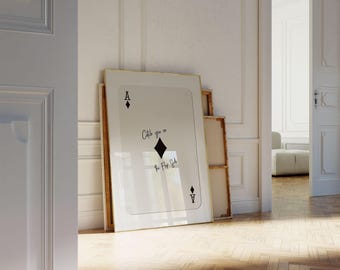 May include: A framed art print resembling an Ace of Diamonds playing card, with the text "Catch you on the Flip Side." The artwork is displayed against a white wall, with a wooden floor in the foreground. Additional framed art pieces are leaning against the wall.