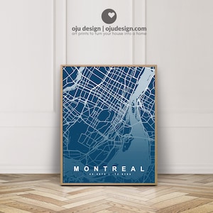 Puede incluir: Una impresión enmarcada del mapa de Montreal, con un degradado azul y líneas blancas que representan calles y vías fluviales. El nombre de la ciudad "MONTREAL" se muestra en blanco en la parte inferior. La impresión está en un marco de madera. El texto "oju design | ojudesign.com art prints to turn your house into a home" está en la parte superior.