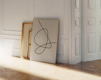 May include: Three framed art pieces leaning against a white wall. The largest piece features a gold frame and a beige background with a black line drawing. The other two pieces have gold frames and beige canvas.