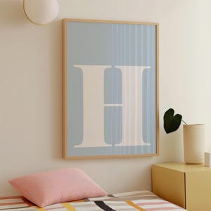 May include: A framed art print featuring a large, light beige letter "H" against a pale blue background. The artwork has a minimalist design with a wooden frame, suitable for home decor.
