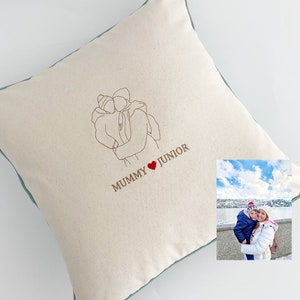 May include: A white cushion with a green border and a line drawing of a person holding another person. The text "MUMMY ♥ JUNIOR" is embroidered on the cushion.