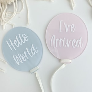 Può includere: Due cartelli rotondi in acrilico per l'annuncio di nascita con nastro bianco. Il cartello blu dice "Hello World" e il cartello rosa dice "I've Arrived".
