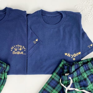 May include: Two navy blue t-shirts with gold text and a pair of green and blue plaid pajama pants. The text on the shirts reads "all I want for christmas..." and "is you".