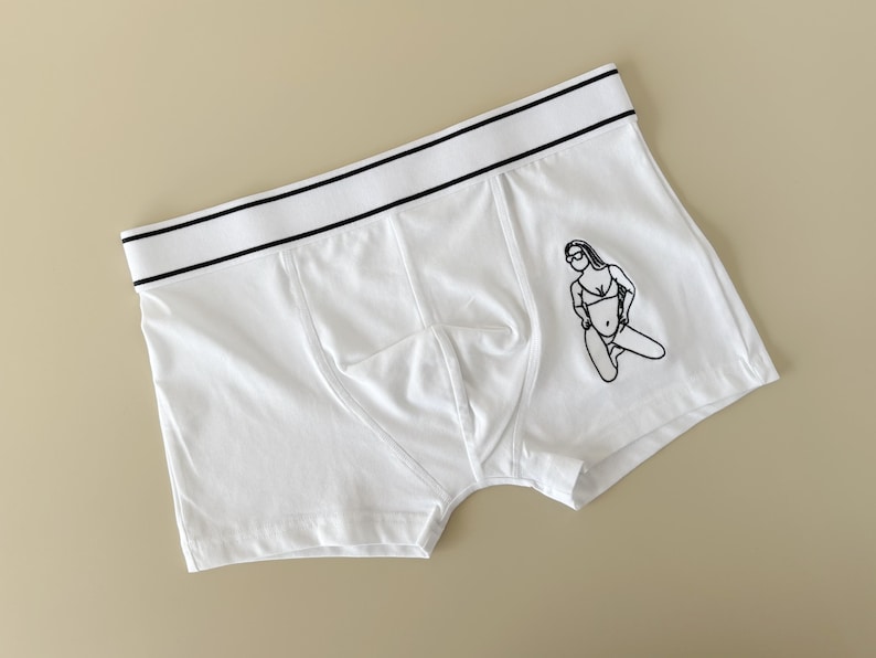 May include: White boxer briefs with a black waistband and a black line drawing of a woman in a bikini on the front.