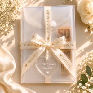 May include: A translucent rectangular envelope secured with a cream-colored ribbon printed with the text OLIVIA & JAMES. A heart-shaped acrylic tag hangs from the ribbon, featuring the text OLIVIA & JAMES and 15.06.2024. A 50 Euro banknote is visible inside.