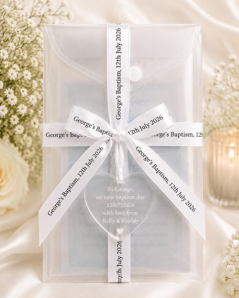 May include: A translucent rectangular envelope secured with a white ribbon printed with the text George's Baptism, 12th July 2026. A clear heart-shaped acrylic ornament hangs from the ribbon, inscribed with To George, on your baptism day 12/07/2026.