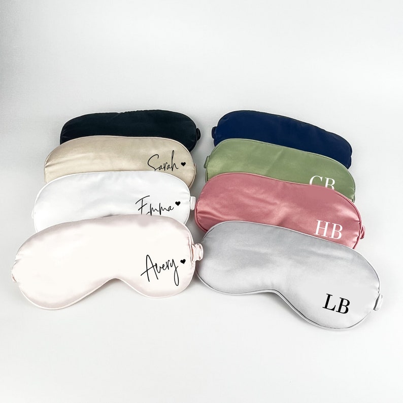 May include: Eight satin sleep masks in various colors with personalized names and initials. The masks are arranged in a row, with the names facing the viewer. The names are "Sarah", "Emma", "Avery", "LB", "HB", "CB", and two blank masks.