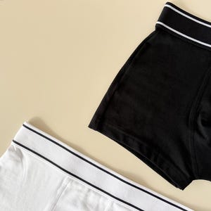 May include: Two pairs of underwear, one black and one white, with a white trim around the waistband.