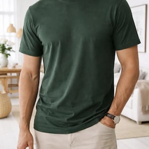 Pode incluir: Uma camiseta verde escuro com gola redonda e cal&ccedil;as c&aacute;qui. A camiseta &eacute; de cor s&oacute;lida e parece ser feita de um material macio. A pessoa est&aacute; usando um rel&oacute;gio com uma pulseira de couro marrom.