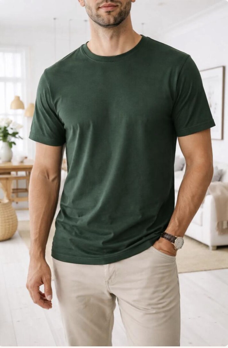 Pode incluir: Uma camiseta verde escuro com gola redonda e cal&ccedil;as c&aacute;qui. A camiseta &eacute; de cor s&oacute;lida e parece ser feita de um material macio. A pessoa est&aacute; usando um rel&oacute;gio com uma pulseira de couro marrom.