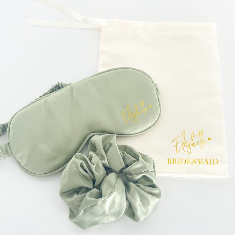 May include: A green satin sleep mask, a green satin scrunchie, and a white drawstring bag with the text "Elizabeth BRIDESMAID" in gold lettering.