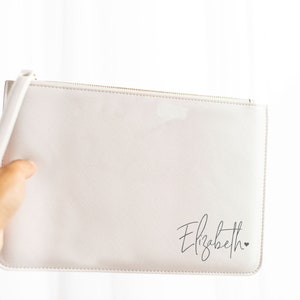 May include: A white zippered pouch with a black cursive inscription that reads "Elizabeth" and a small heart.