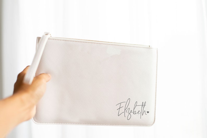 May include: A white zippered pouch with a black cursive inscription that reads "Elizabeth" and a small heart.