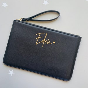 Peut inclure: Pochette en cuir noir avec une fermeture &eacute;clair dor&eacute;e et une inscription dor&eacute;e qui dit "Eden" avec un petit c&oelig;ur.