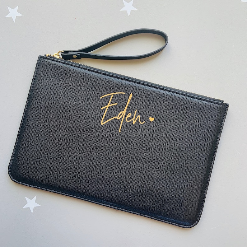 Peut inclure: Pochette en cuir noir avec une fermeture &eacute;clair dor&eacute;e et une inscription dor&eacute;e qui dit "Eden" avec un petit c&oelig;ur.