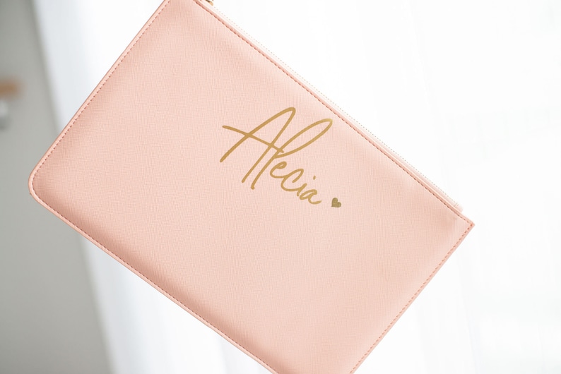 May include: A pale pink zippered pouch with the name "Alecia" written in gold script with a small gold heart.