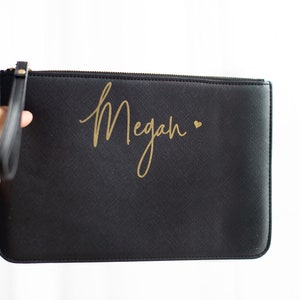 May include: Black clutch bag with a gold zipper and a gold inscription that reads "Megan" with a small heart.