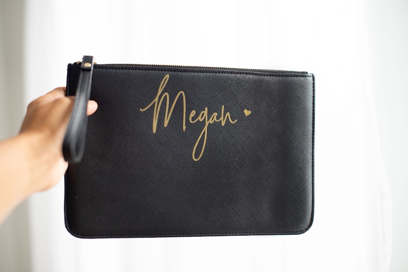 May include: Black clutch bag with a gold zipper and a gold inscription that reads "Megan" with a small heart.