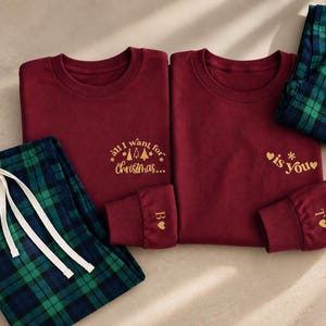Könnte beinhalten: Zwei kastanienbraune Langarmshirts mit goldener Schrift und grün-blauer karierter Schlafanzughose. Das linke Shirt zeigt "all I want for Christmas..." mit Baum-Symbolen, das rechte "is you" mit Herzen. An den Ärmelbündchen befinden sich die Buchstaben B und T.