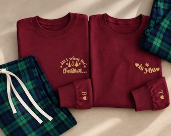 May include: Two maroon long-sleeve shirts with gold text and green and blue plaid pajama pants. The left shirt reads "all I want for Christmas..." with tree icons, and the right shirt reads "is you" with hearts. The cuffs feature the letters B and T.