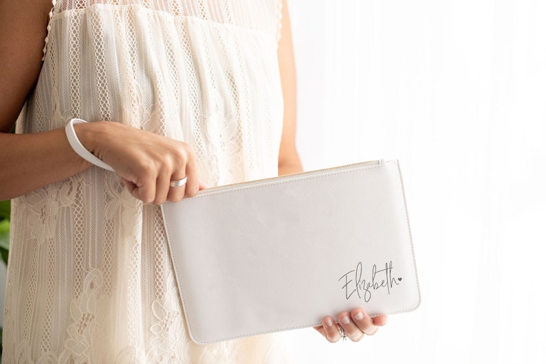 May include: White zippered clutch with a gold zipper and the name "Elizabeth" written in cursive with a small heart.