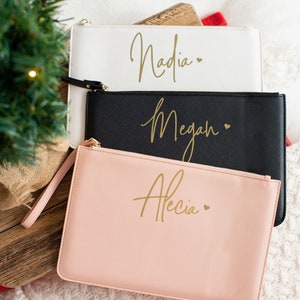 May include: Three personalized cosmetic bags with gold lettering. The bags are white, black, and pink. The names on the bags are Nadia, Megan, and Alecia.