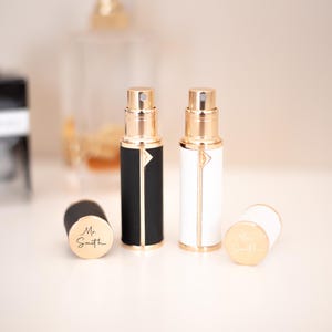 May include: Two refillable perfume atomizers, one black and one white, with gold accents and caps. The atomizers are on a white surface and have a gold label that says "Mr. Smith".
