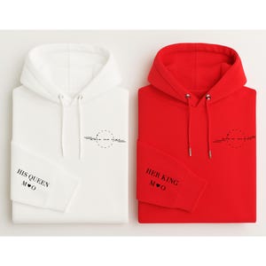 May include: Two hooded sweatshirts, one white and one red. The white sweatshirt has "HIS QUEEN" printed on the sleeve, and the red sweatshirt has "HER KING" printed on the sleeve. Both have a black graphic on the chest.