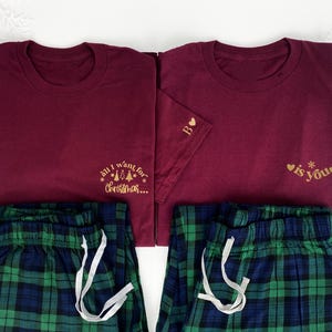 Op de afbeelding: Bordeauxkleurige bijpassende pyjamasets. Elke set bevat een shirt met korte mouwen met gouden tekst en een geruite pyjamabroek. Eén shirt zegt "all I want for Christmas..." en de andere "is you". De broek is blauw, groen en wit geruit.